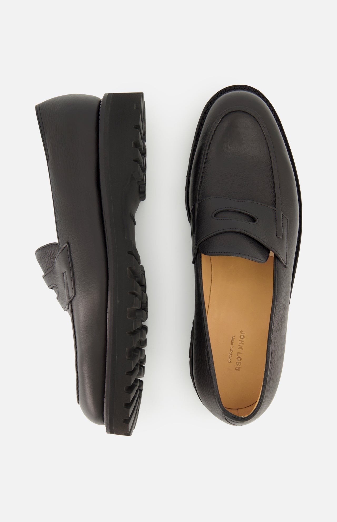The Lopez Gentle Grain Loafer by JOHN LOBB is showcased against a white background, featuring one black leather loafer handmade in England displayed from the side to highlight its textured sole, while the other is shown from above to reveal the tan insole and sleek design.
