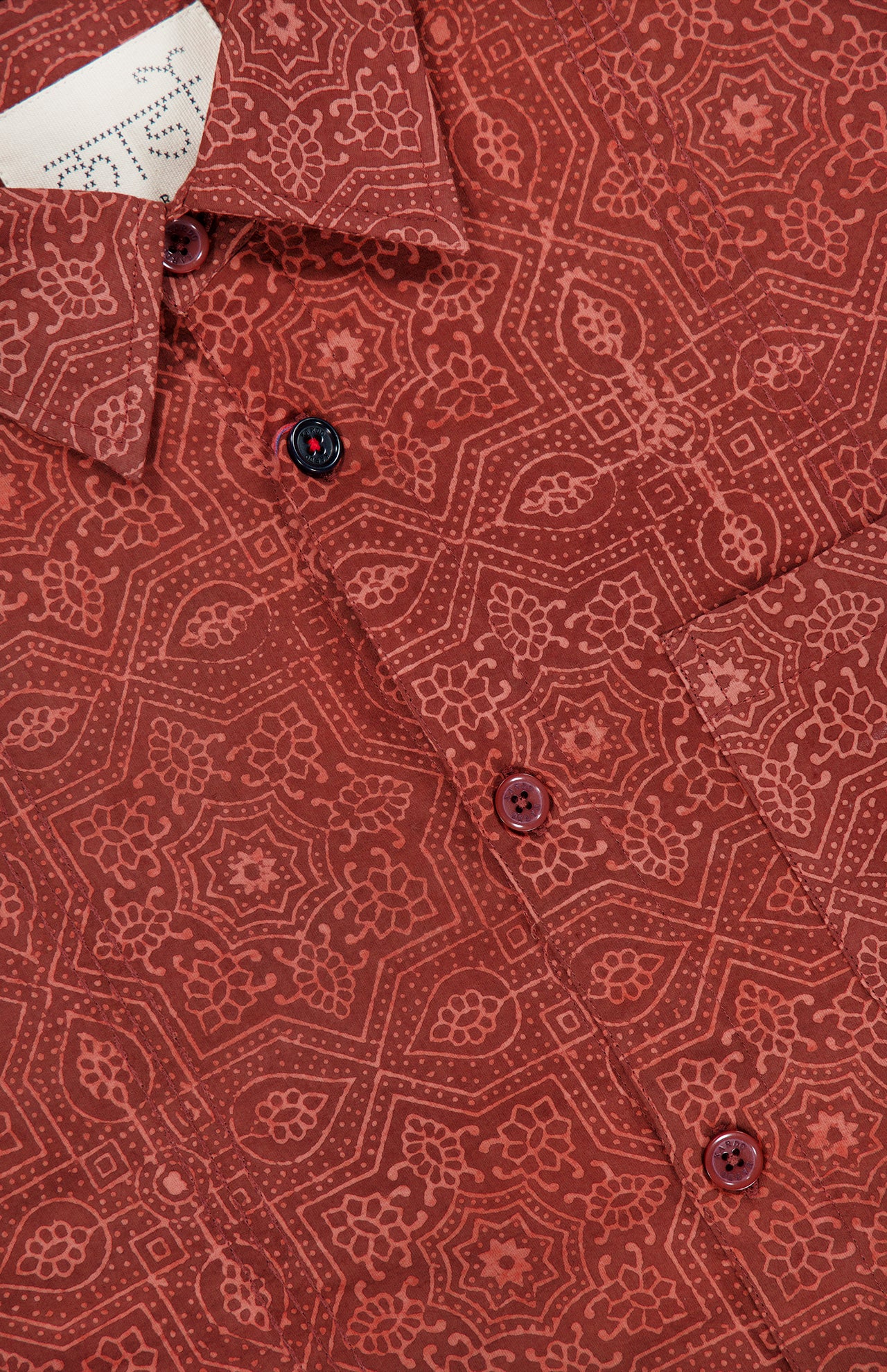 A close-up of the KARDO Luis Oversized Long Sleeve Shirt in brick red showcases its intricate geometric and floral pattern, with buttons visible along the placket.