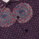 A close-up of the KARDO Martin Relaxed Fit Long Sleeve Shirt in purple, showcasing small white polka dots, dark buttons, and circular blue and red designs near the collar and chest. A portion of a white label with red stitching is also visible.