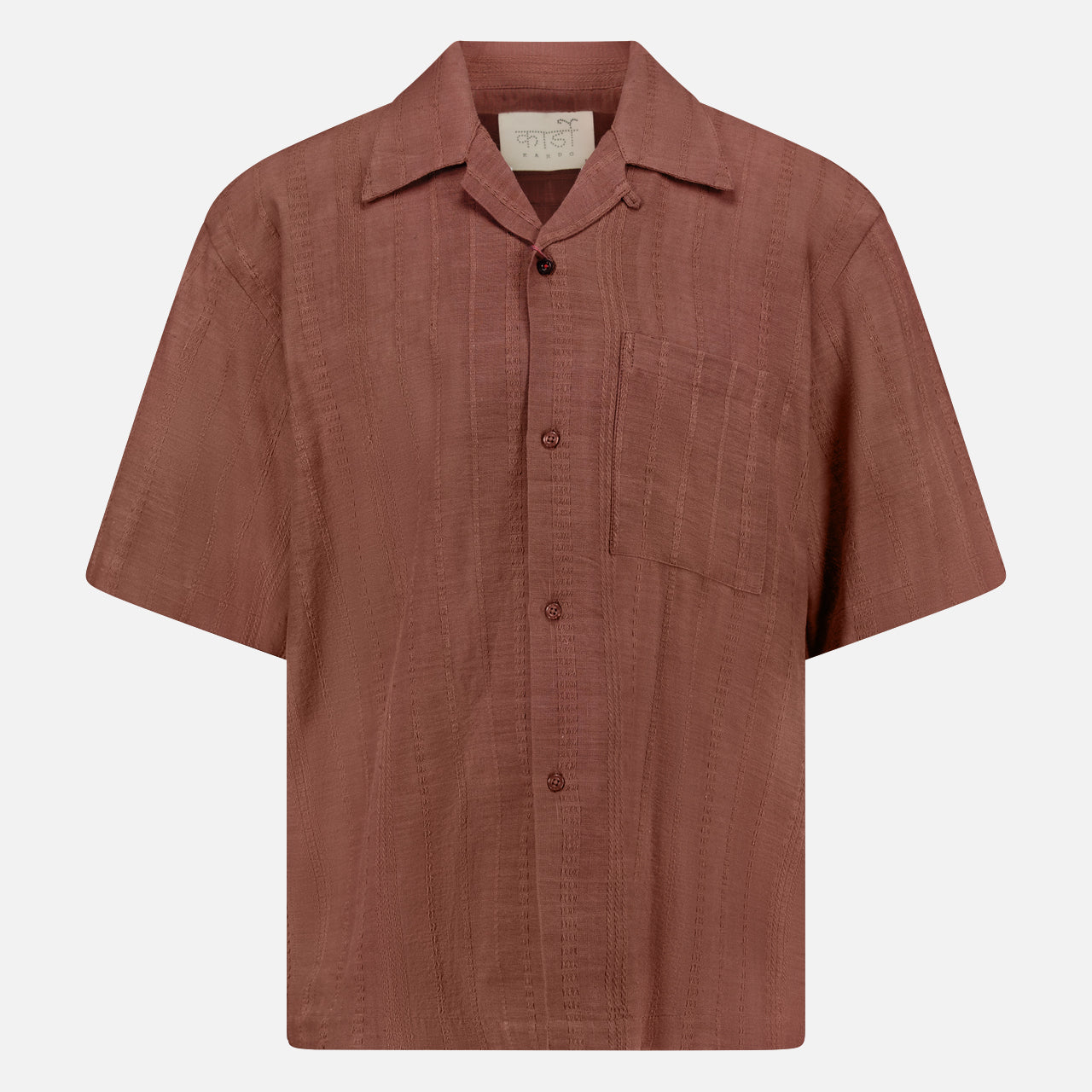 The KARDO Rohit Stripe Short Sleeve Shirt is a brown, 100% cotton, oversized button-up with a chest pocket, collar, and subtle textured stripes. Displayed on a plain white background.