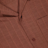 Close-up of the KARDO Rohit Stripe Short Sleeve Shirt in brown 100% cotton, featuring a subtle stripe pattern, oversized fit, chest pocket, visible buttons, and a partially visible white label at the collar.