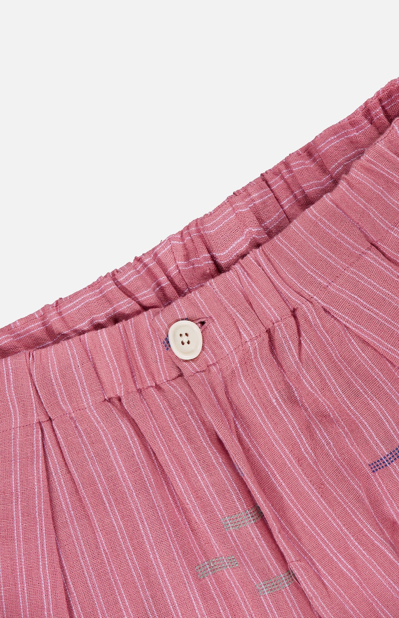 Close-up of the waistband of KARDO's Taka Striped Trouser Pants, showing relaxed fit in pink with vertical white stripes, a white button, elastic waistband, and lightweight textured fabric.