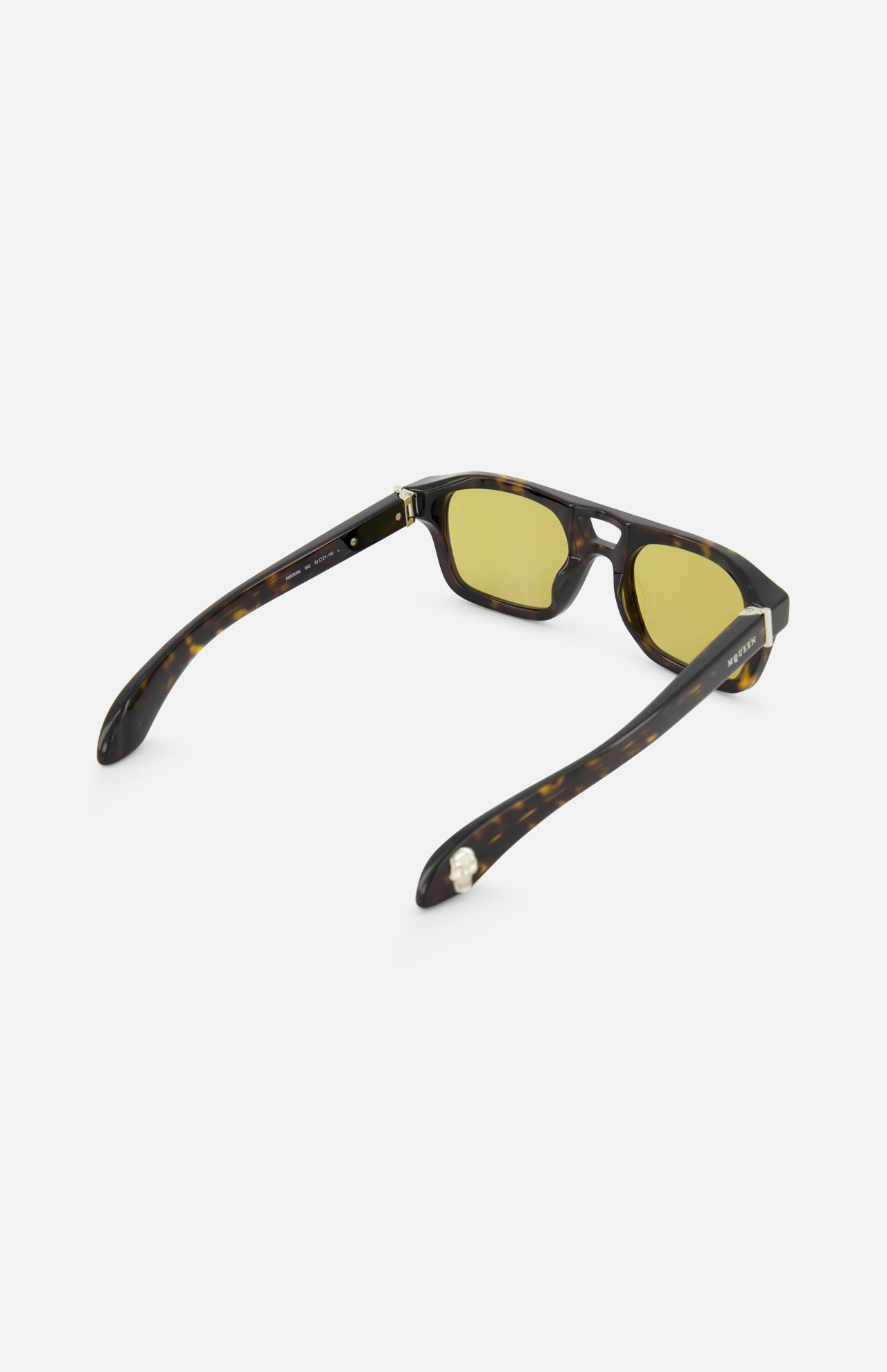 The Alexander McQueen Pilot Brown Sunglasses by ALEXANDER MCQUEEN are shown from a rear angle on a white background, featuring dark tortoiseshell frames, yellow-tinted lenses, open arms with metal hinges, and classic pilot style detailing.