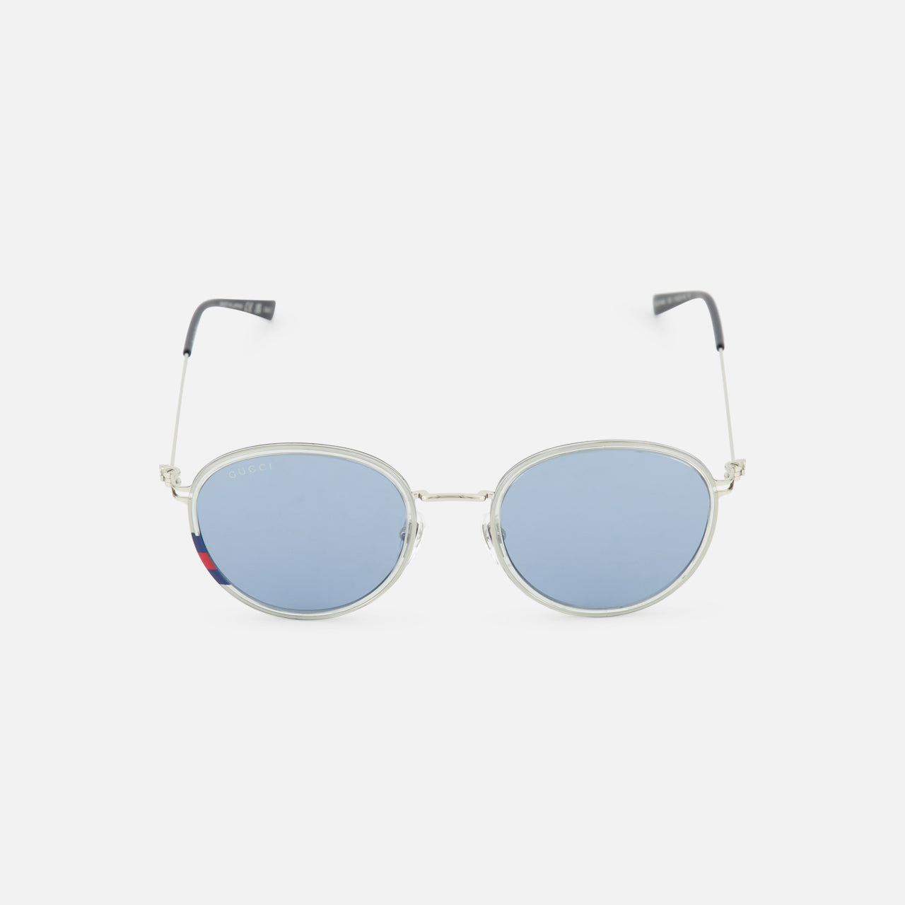The Gucci Round Silver Sunglasses by GUCCI feature silver metal round frames, light blue tinted lenses, and black-tipped arms. These unisex sunglasses are displayed on a plain white background.