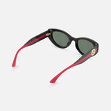 The Gucci Cat Eye Black Sunglasses by GUCCI feature dark tinted lenses, red-green striped arms, and a solid red interior with a gold circular logo. These designer frames stand out against a crisp white background.
