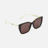The GUCCI Brown Tortoiseshell Sunglasses feature cat-eye frames, dark lenses, gold arms, and pearl accents for a chic look. These sunglasses are displayed on a white background.