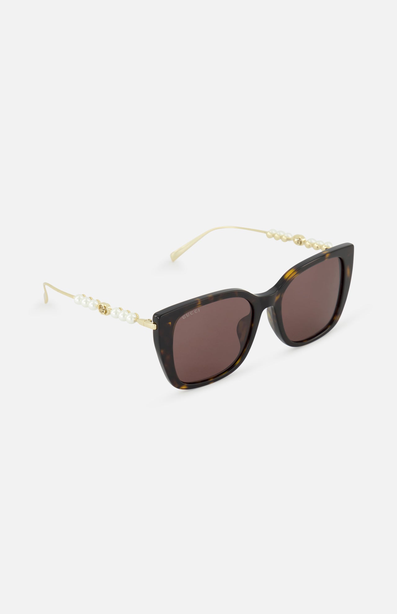 The GUCCI Brown Tortoiseshell Sunglasses feature cat-eye frames, dark lenses, gold arms, and pearl accents for a chic look. These sunglasses are displayed on a white background.