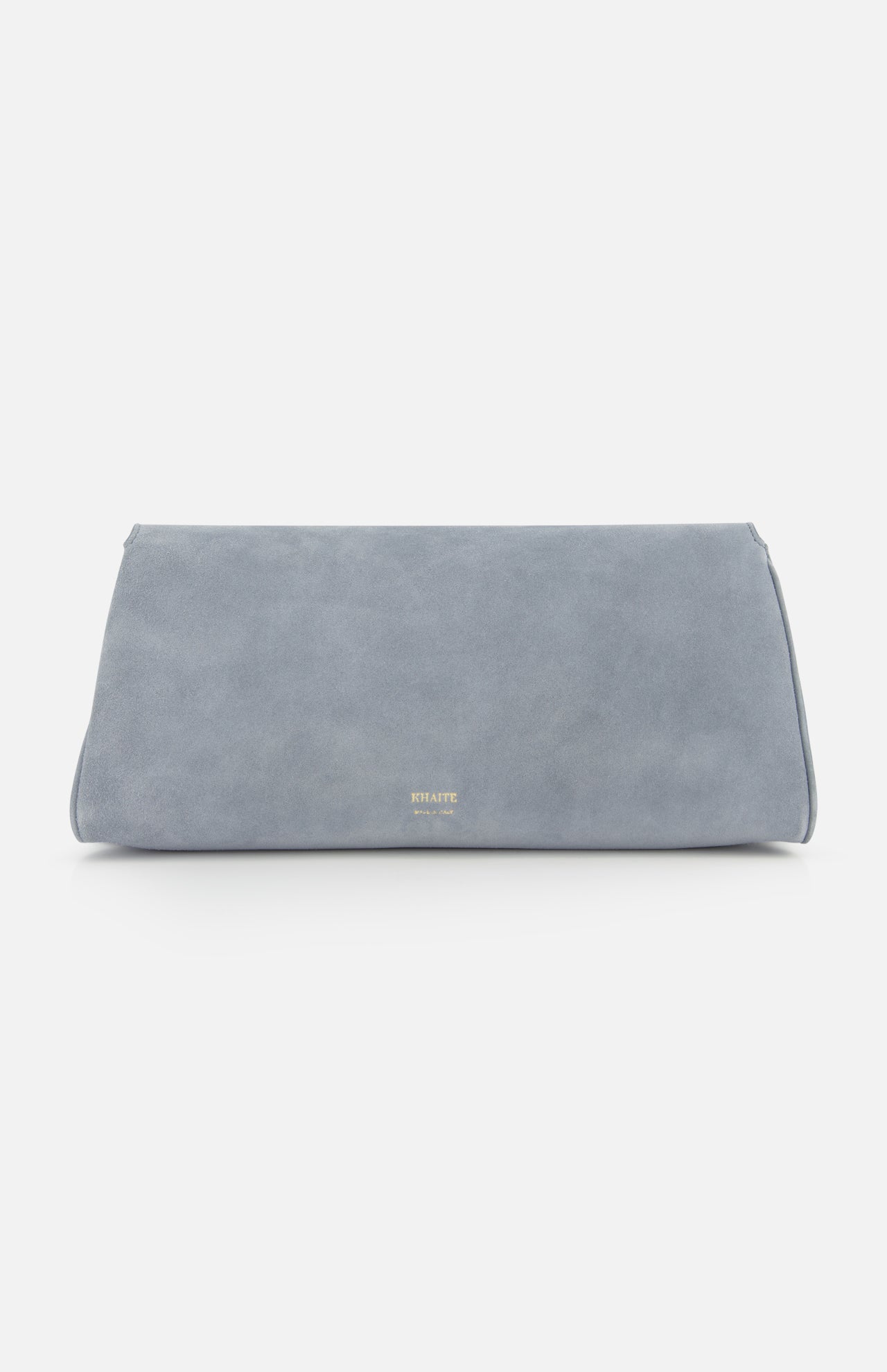 The Audrey Art Deco Suede Clutch by KHAITE is a minimalist, rectangular pale blue bag with Art Deco-inspired hardware and small gold lettering near the bottom center, shown on a plain white background.