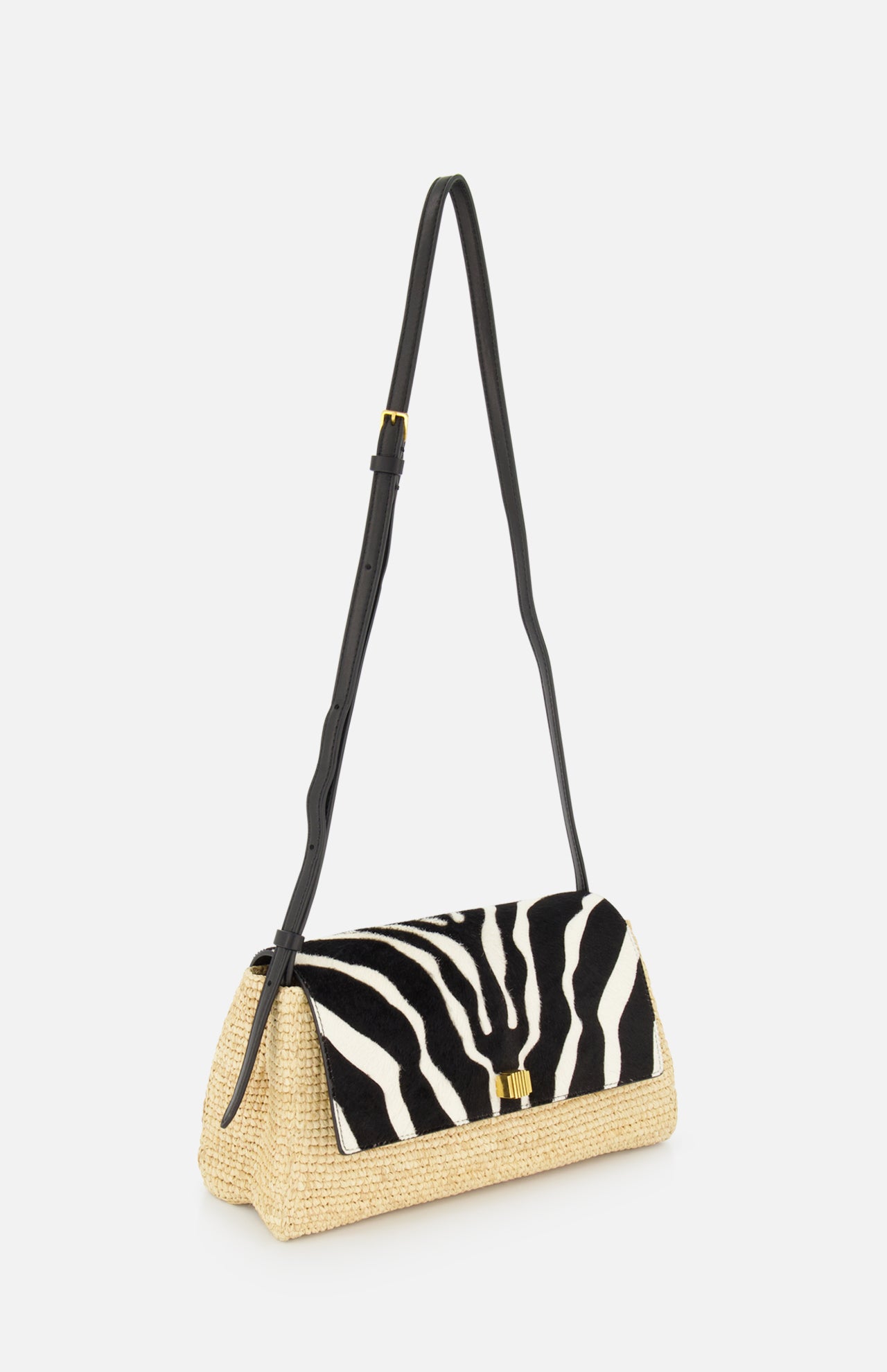 The Audrey Raffia Crossbody Bag by KHAITE features a handwoven straw base from Madagascar, a black and white animal print flap, a small gold front clasp, and a long adjustable black leather strap.