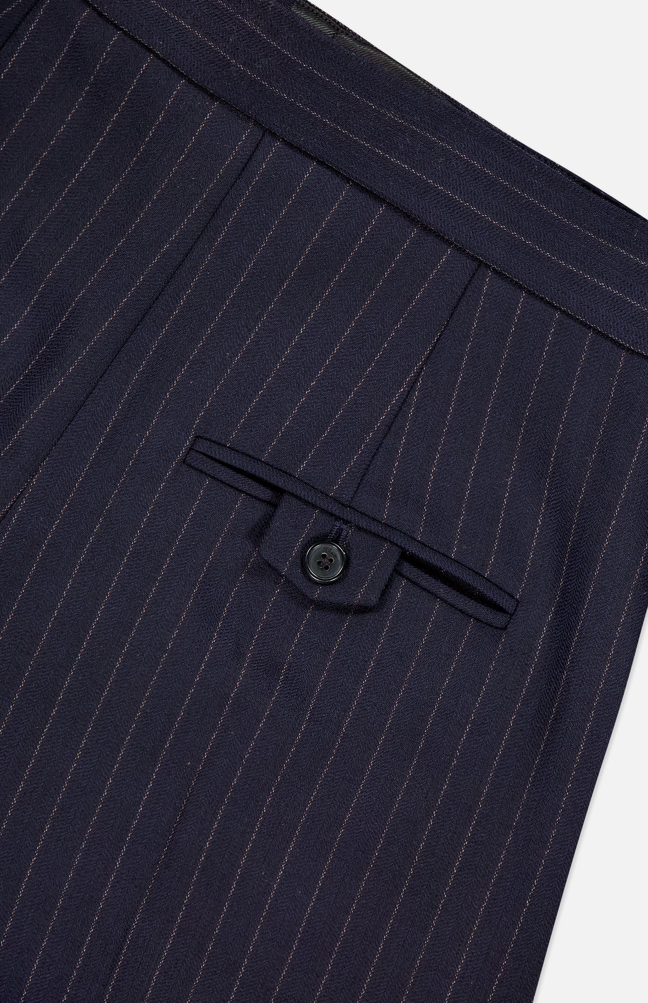 Close-up of the KHAITE Jude Striped Wool-blend Pant in navy, featuring pleats, a button-flap back pocket, and thin light stripes—a classic choice for minimalist wardrobes.