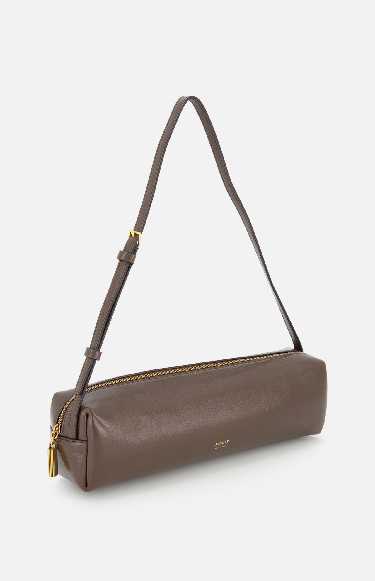 The KHAITE Kye Patent Leather Shoulder Bag features brown patent leather, a gold zipper, and an adjustable strap, shown against a white background.