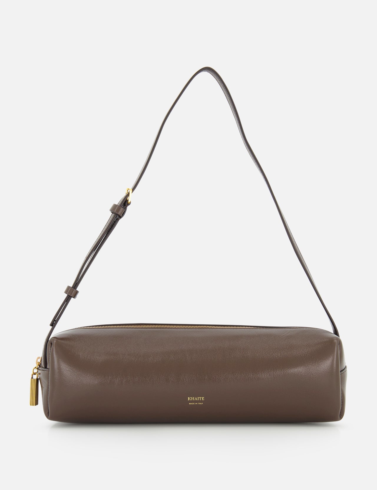 The KHAITE Kye Patent Leather Shoulder Bag features brown patent leather, a cylindrical shape, adjustable strap, gold zipper, and a small gold logo at the front center. It is shown against a white background.