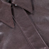 Close-up of the Shelman Leather Bomber Jacket by KHAITE, shown in dark brown lambskin with a pointed collar, visible stitching, and a label displaying the KHAITE brand name in the top left corner.