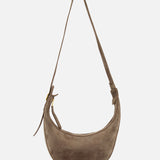 The Augustina Small Crossbody Bag by KHAITE is a light brown suede bag with a curved zip-top hobo silhouette, adjustable strap, gold hardware, and embossed logo on the front—crafted in Italy and shown on a white background.