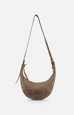 The Augustina Small Crossbody Bag by KHAITE is a light brown suede bag with a curved zip-top hobo silhouette, adjustable strap, gold hardware, and embossed logo on the front—crafted in Italy and shown on a white background.