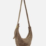 The Augustina Small Crossbody Bag by KHAITE features light brown suede in a crescent, zip-top hobo silhouette with a long adjustable strap and gold-tone hardware. Made in Italy, it's shown against a plain white background.
