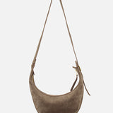 The KHAITE Augustina Small Crossbody Bag is a light brown suede crescent-shaped bag with a zip-top hobo silhouette, long adjustable strap, and gold-tone zipper, shown against a plain white background.