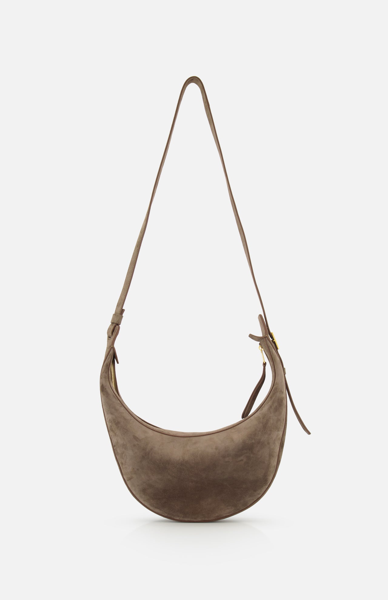 The KHAITE Augustina Small Crossbody Bag is a light brown suede crescent-shaped bag with a zip-top hobo silhouette, long adjustable strap, and gold-tone zipper, shown against a plain white background.