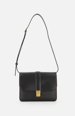 The KHAITE Blake Leather Crossbody Bag highlights Italian craftsmanship with sleek black leather, a gold rectangular flap clasp, and a single adjustable strap. Its minimalist, elegant design stands out against a plain white background.