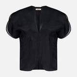 The KHAITE Briar Notch Neck Silk Blouse, featuring a black hue with short, rounded structured sleeves and a deep V-neckline, epitomizes quiet luxury. Expertly crafted in Italy from lustrous satin silk, it is showcased elegantly against a plain white background.