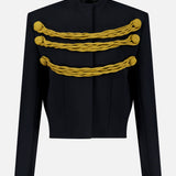The Cord Embroidery York Jacket by KHAITE is a black, structured military-inspired piece with a high collar, distinguished by two rows of thick yellow braided trim with rosette ends across the chest and detailed gold cord embroidery for added distinction.