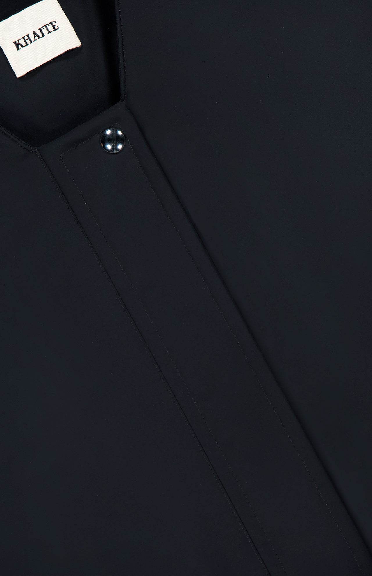 Close-up of the KHAITE Cordan Cropped Bomber Jacket in black, featuring a snap button and a visible KHAITE label in the top left corner—a perfect addition to any minimalist wardrobe.