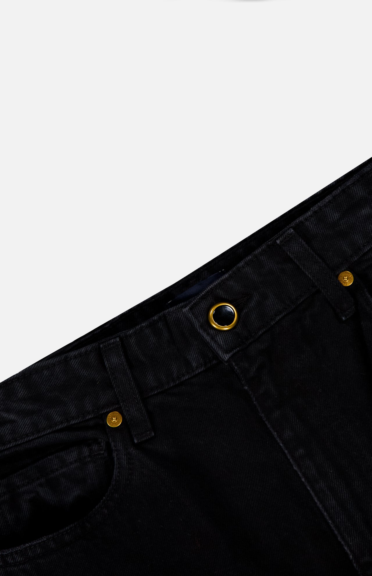 Close-up of the waistband and front pocket of the KHAITE Danielle Jean in Prescott, a high-rise black style with gold metal button, rivet, and grommet details, shown against a light gray background.