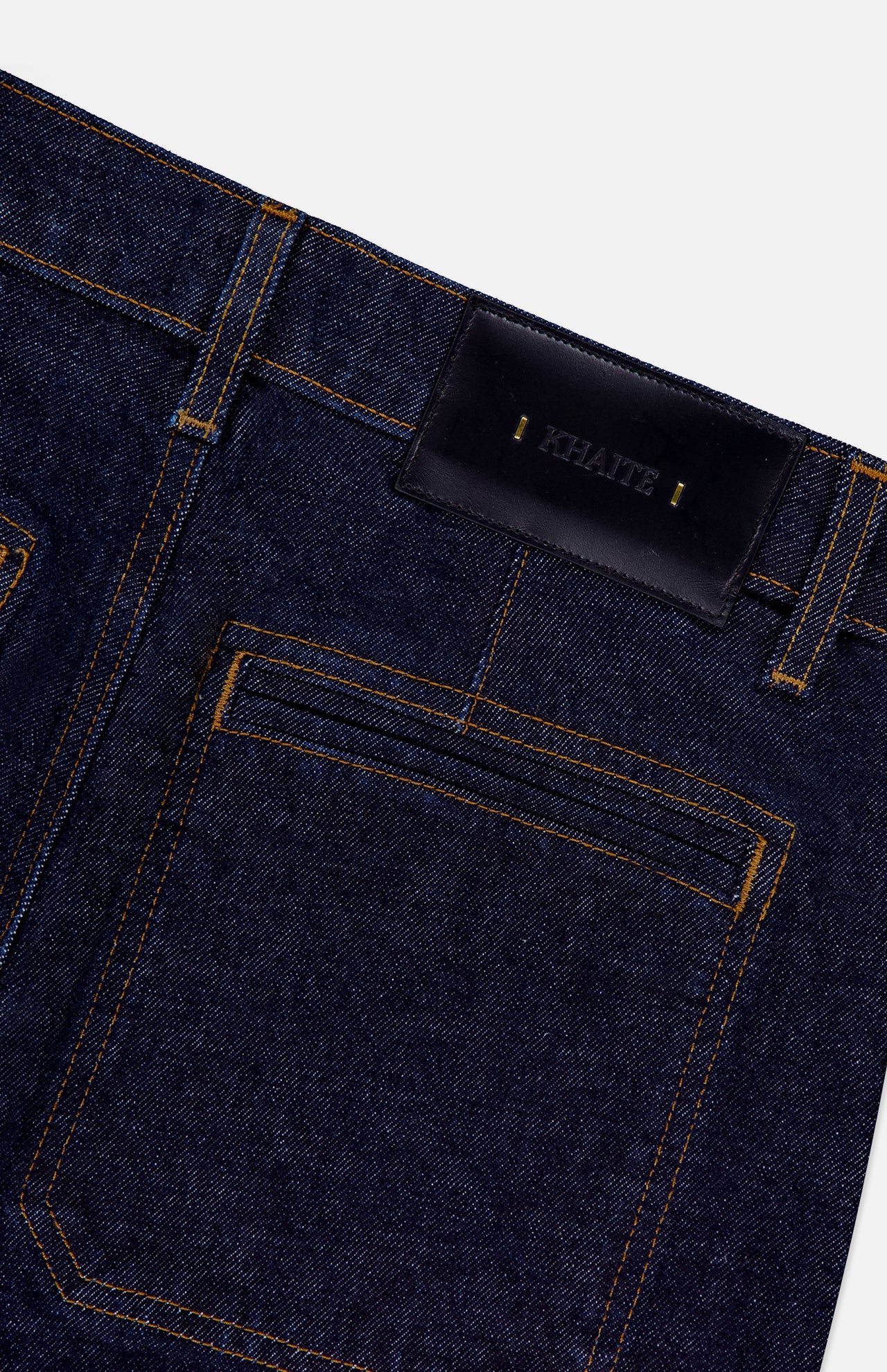 Close-up of the back pocket and waistband of the KHAITE Delmonico Wide Leg Jean in Benson, featuring a high-waisted, dark wash design with yellow stitching and a black leather patch stamped with the brand name in gold letters.