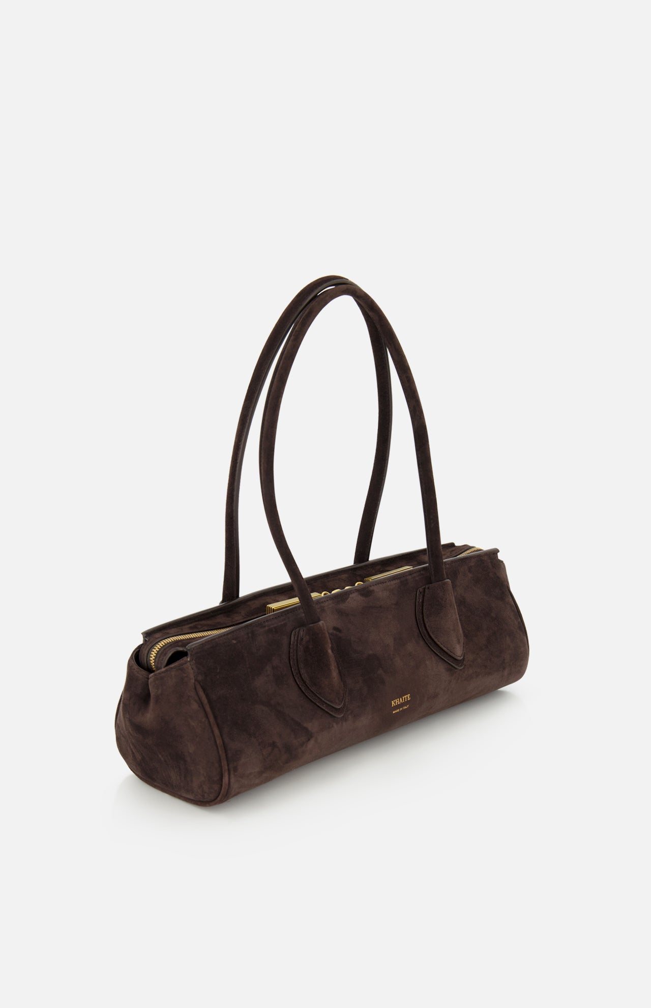 The KHAITE Donna Soft Handbag is a dark brown suede bag crafted in Italy, featuring two long straps, a gold zipper, and gold logo text on the front. It boasts a rectangular, structured silhouette with a minimalist and elegant design, photographed against a plain white background.