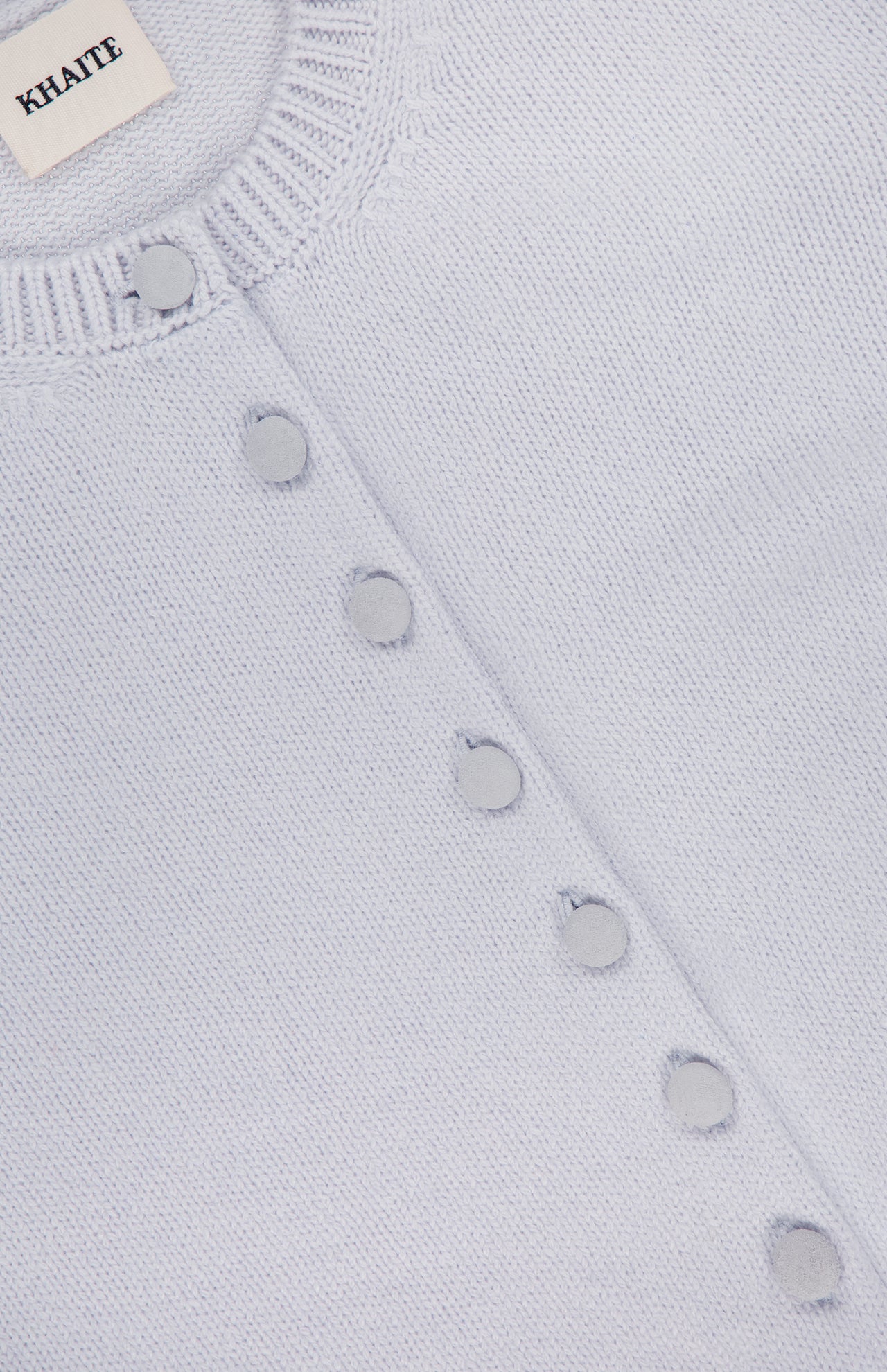 Close-up of the KHAITE Everheart Suede Button Cardigan in light blue, featuring a ribbed neckline, suede-covered buttons set diagonally, and the KHAITE label inside the collar—perfect for a minimalist wardrobe.
