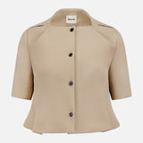 The KHAITE Folded Neck Franc Jacket is a beige Italian crepe peplum style with short sleeves, structured collar, flared hem, and black buttons, featuring a label inside the neckline. Shown on a plain white background—ideal for minimalist wardrobes.