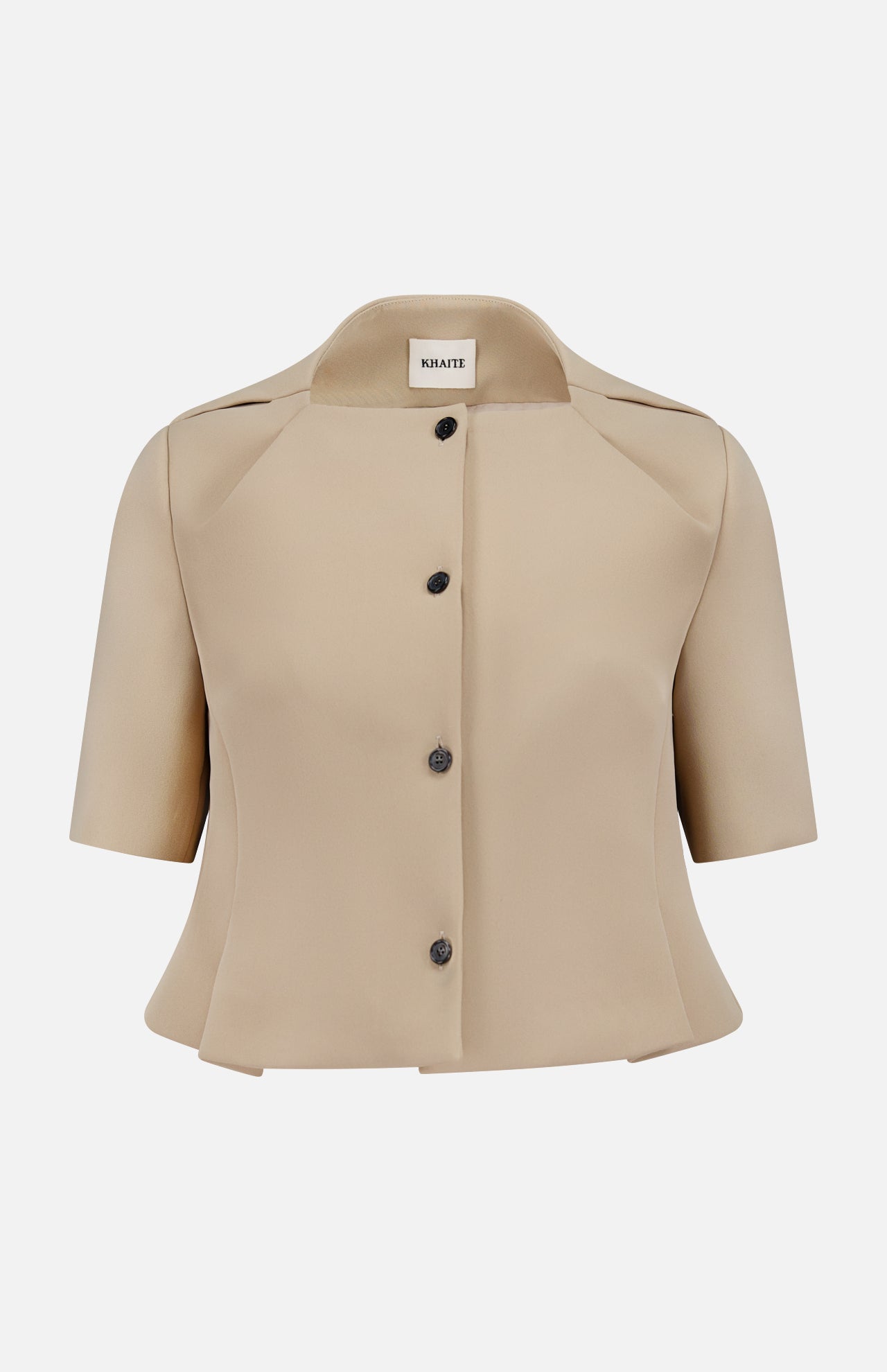 The KHAITE Folded Neck Franc Jacket is a beige Italian crepe peplum style with short sleeves, structured collar, flared hem, and black buttons, featuring a label inside the neckline. Shown on a plain white background—ideal for minimalist wardrobes.