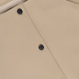 Close-up of the Folded Neck Franc Jacket by KHAITE, crafted from smooth beige Italian crepe with black buttons and a white brand label at the collar—an ideal choice for a minimalist wardrobe.