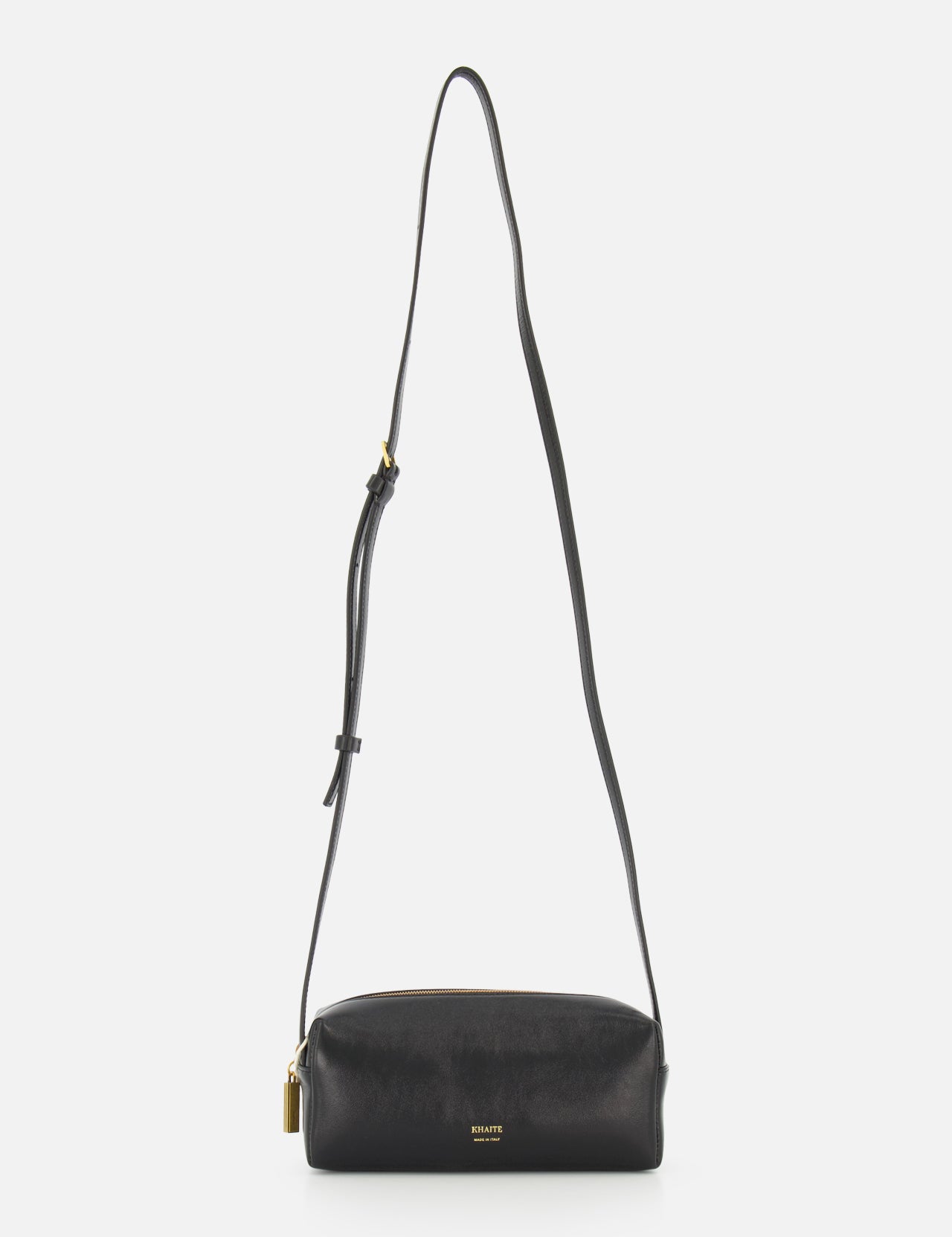 The KHAITE Kye Mini Crossbody Bag in black patent leather features a long adjustable strap, gold-tone hardware, and a small padlock detail, shown against a plain white background.