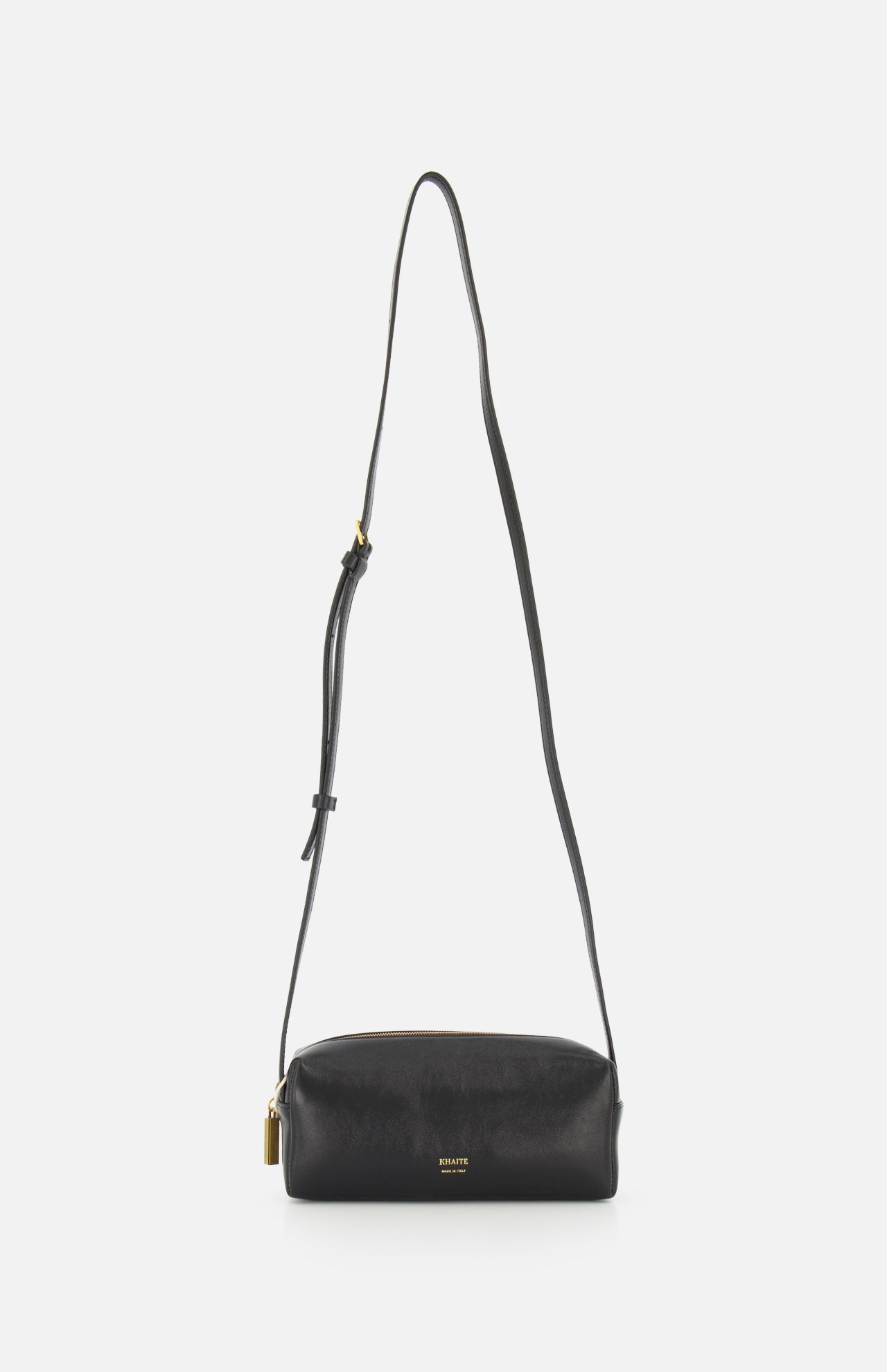 The KHAITE Kye Mini Crossbody Bag in black patent leather features a long adjustable strap, gold-tone hardware, and a small padlock detail, shown against a plain white background.