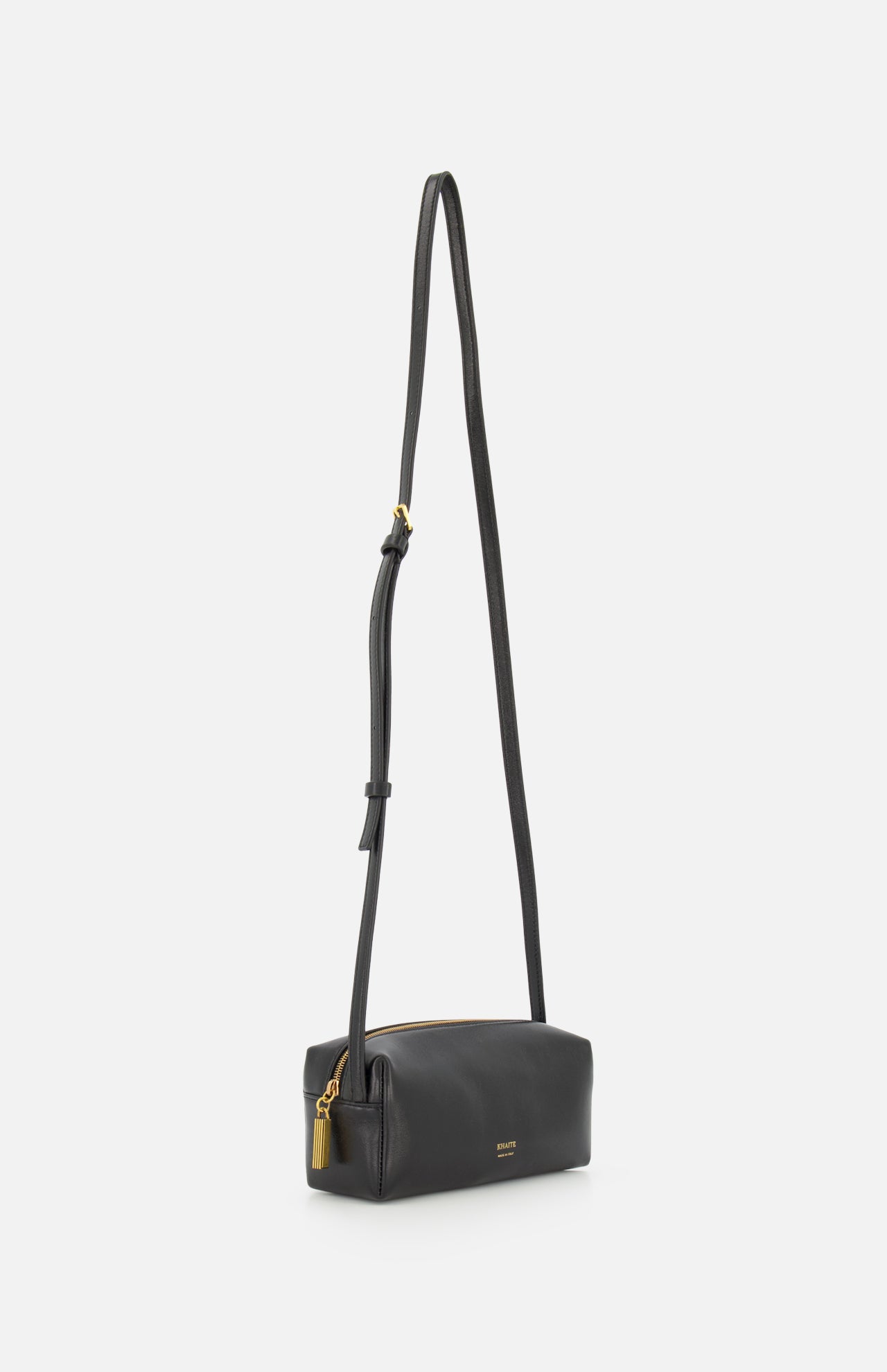 The KHAITE Kye Mini Crossbody Bag is a small black Italian-made bag with sleek leather, a long adjustable strap, gold zipper and charm, minimalistic design, and subtle branding near the bottom.