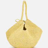 The Lotus Viscose Raffia Medium Bag by KHAITE is a yellow tote crafted from sustainably harvested raffia, featuring a slouchy, rounded silhouette and two handles, shown against a plain white background.
