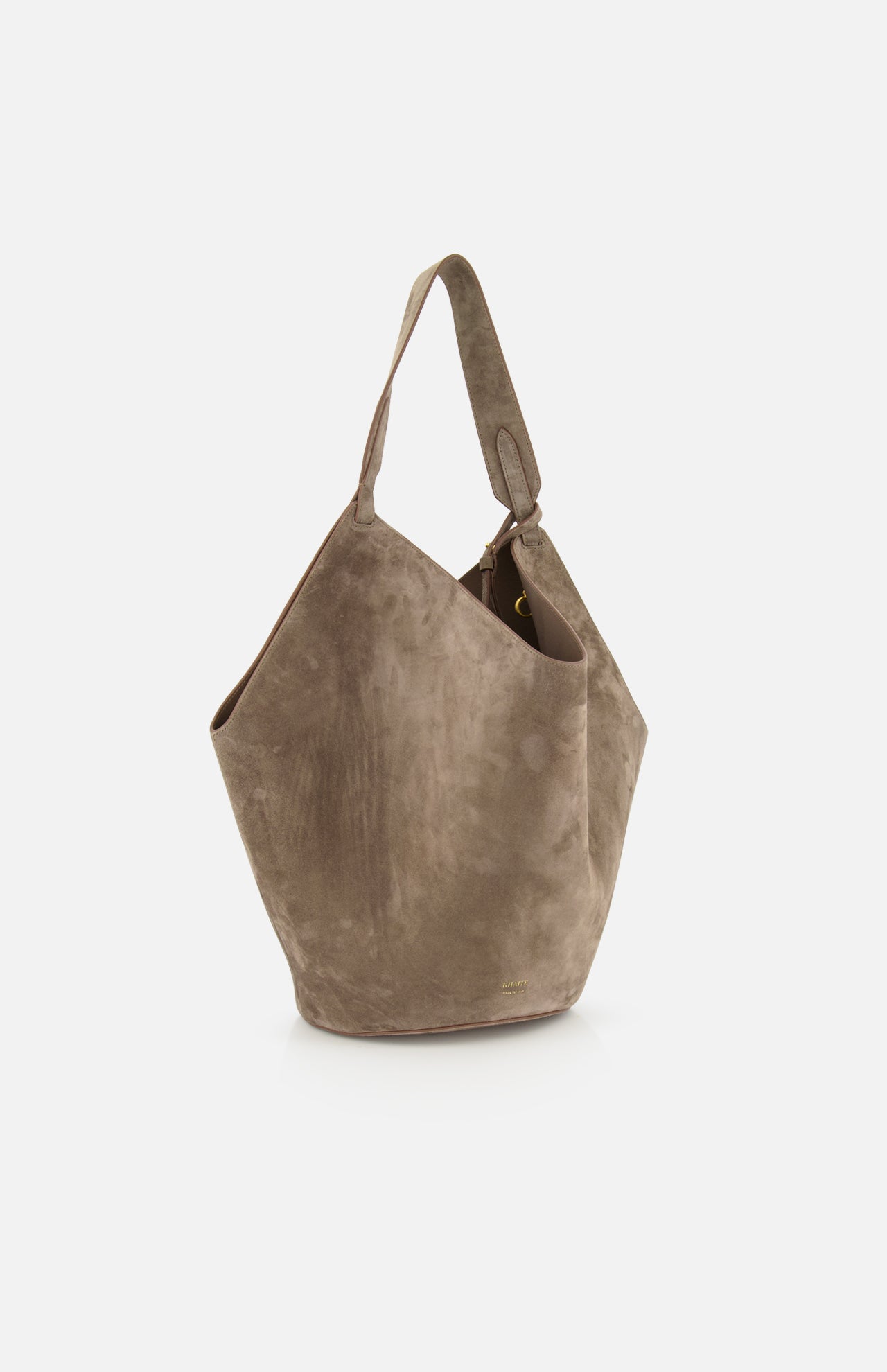 The KHAITE Lotus Medium Suede Tote Bag features taupe suede, a wide single shoulder strap, a soft slouchy geometric shape, and includes a removable pouch. Shown against a plain white background.