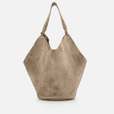 The Lotus Medium Suede Tote Bag by KHAITE is a large, lightweight taupe tote in suede, featuring a wide, angular shape, single top handle with decorative buckle, and a removable pouch. Displayed on a plain white background.
