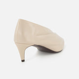 The Miriam Glazed Leather Pump 50 by KHAITE features beige nude glazed leather with a subtle wrinkled texture and a pointed toe heel, shown from the back and side on a white background—ideal for minimalist style.