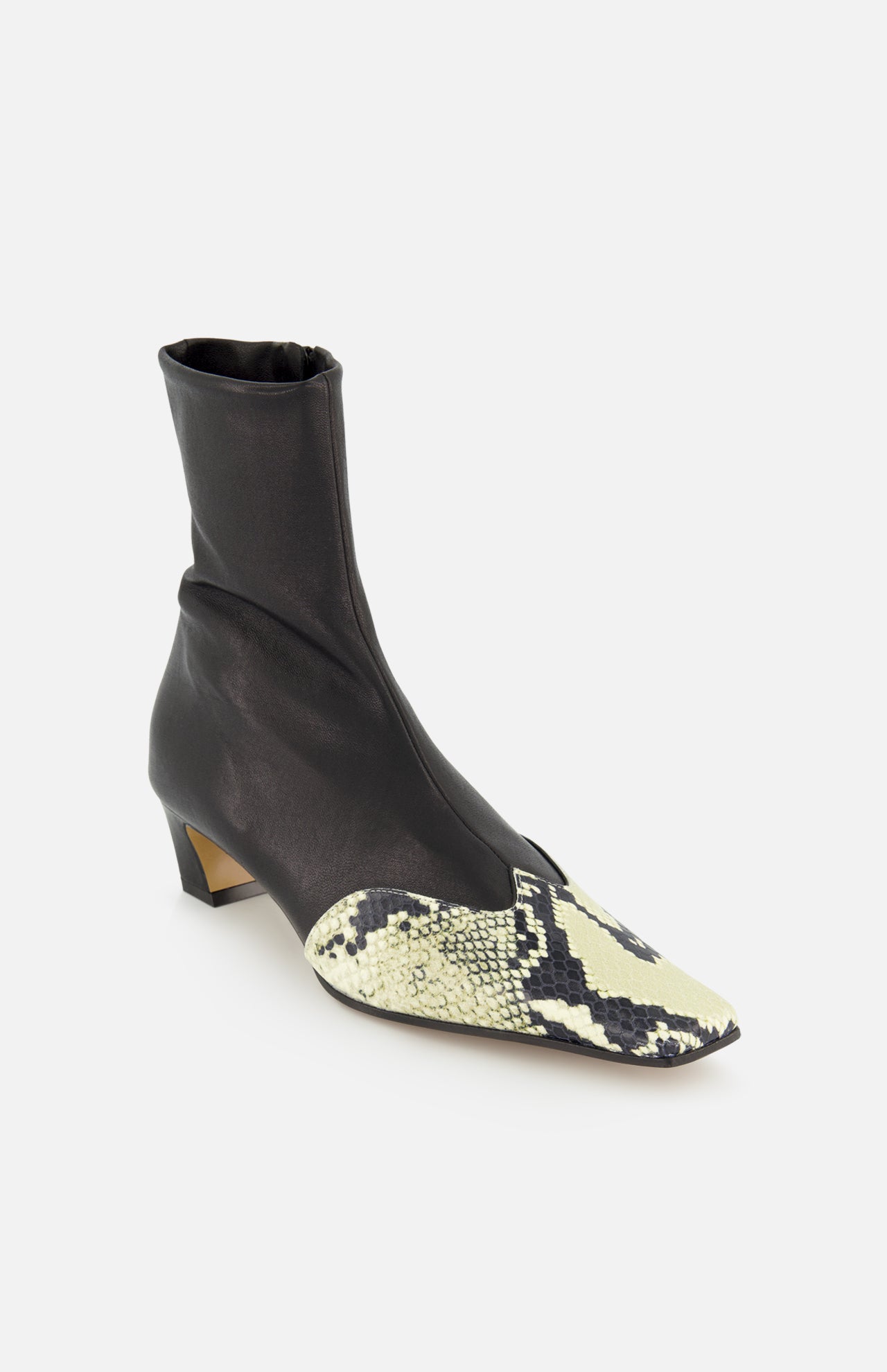 The Nevada Ankle Stretch Boot in Python by KHAITE is a pointed-toe black cowboy boot with a low heel, crafted from black leather and detailed with beige and black python print wingtips, shown on a white background.