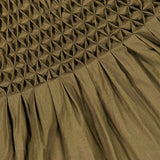 The Nola Smocked Waist Dress by KHAITE is an olive green organic cotton dress with a textured, geometric diamond-shaped hand-smocked waist on the upper section, seamlessly transitioning into smooth pleats along the lower section.