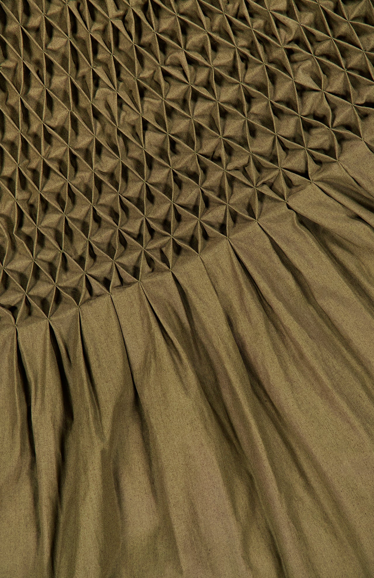 The Nola Smocked Waist Dress by KHAITE is an olive green organic cotton dress with a textured, geometric diamond-shaped hand-smocked waist on the upper section, seamlessly transitioning into smooth pleats along the lower section.