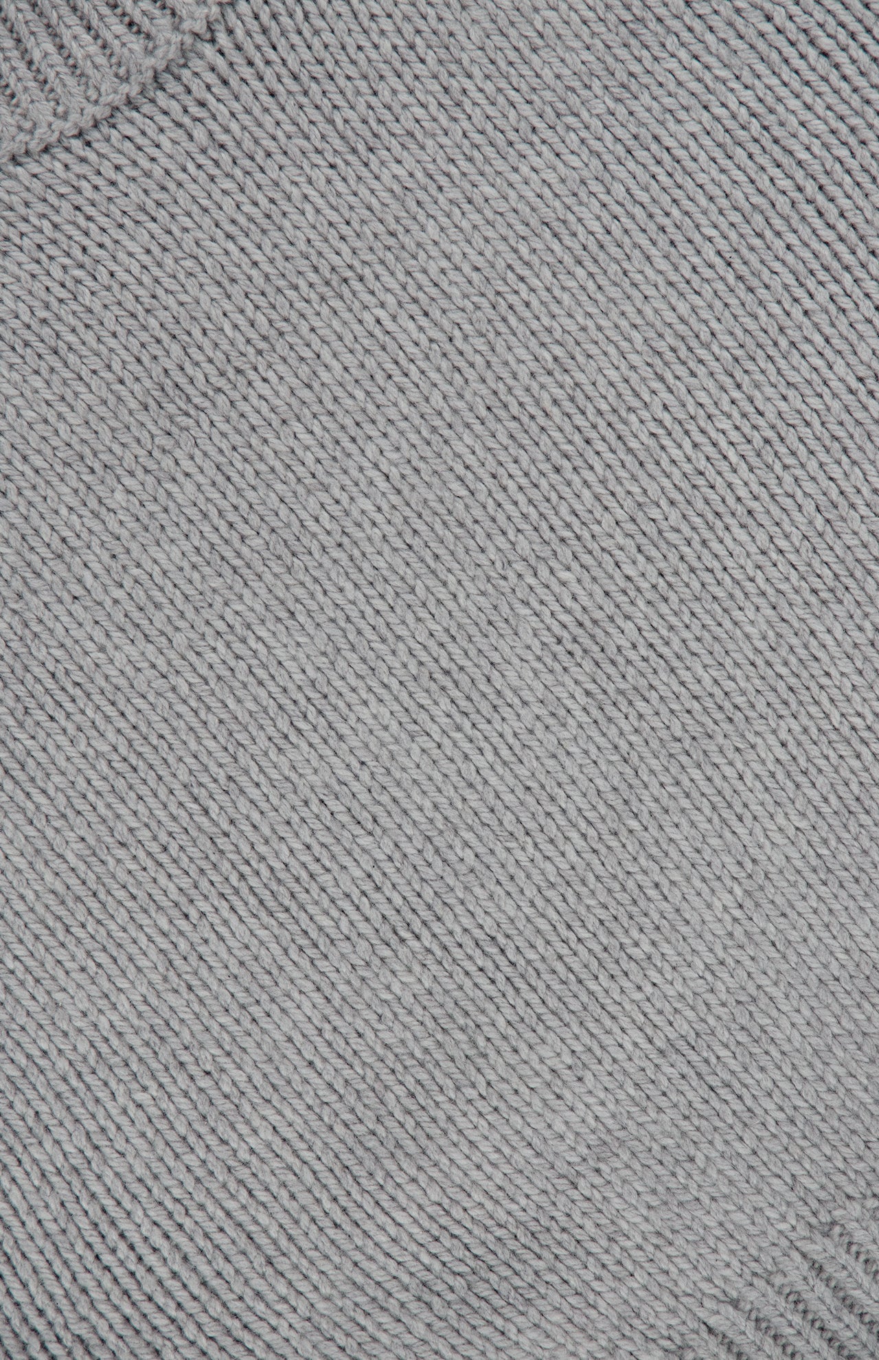 Close-up of the light gray textured fabric of the KHAITE Phelps Cashmere Sweater, featuring diagonal ribbed lines that form a pattern of small, evenly spaced ridges—an elegant detail that adds understated appeal to any minimalist wardrobe.