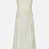 The Raina Ruched Midi Dress by KHAITE is an ivory silk charmeuse dress featuring a sleeveless silhouette, delicate spaghetti straps, and ruched detailing on the bodice. This midi dress flares gently with a subtle sheer finish and is photographed against a plain white background.