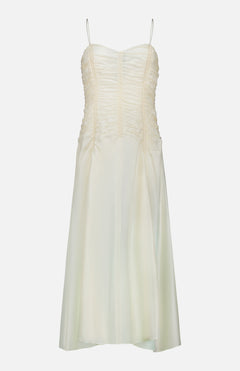The Raina Ruched Midi Dress by KHAITE is an ivory silk charmeuse dress featuring a sleeveless silhouette, delicate spaghetti straps, and ruched detailing on the bodice. This midi dress flares gently with a subtle sheer finish and is photographed against a plain white background.