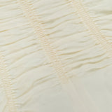 Close-up of light beige ruched fabric with horizontal stitching lines, creating gathered, textured sections across the material—perfectly exemplified by the KHAITE Raina Ruched Midi Dress.