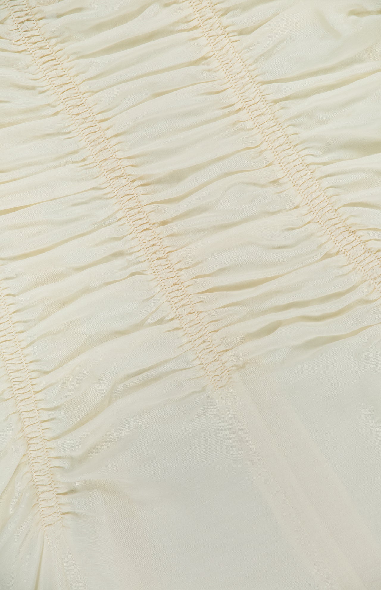 Close-up of light beige ruched fabric with horizontal stitching lines, creating gathered, textured sections across the material—perfectly exemplified by the KHAITE Raina Ruched Midi Dress.