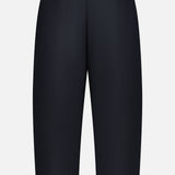 The KHAITE Roma Cropped Pull-on Pant is shown from the back, featuring a plain black design with an elastic waistband, straight leg cut, and lightweight wool suiting—no visible pockets or embellishments.