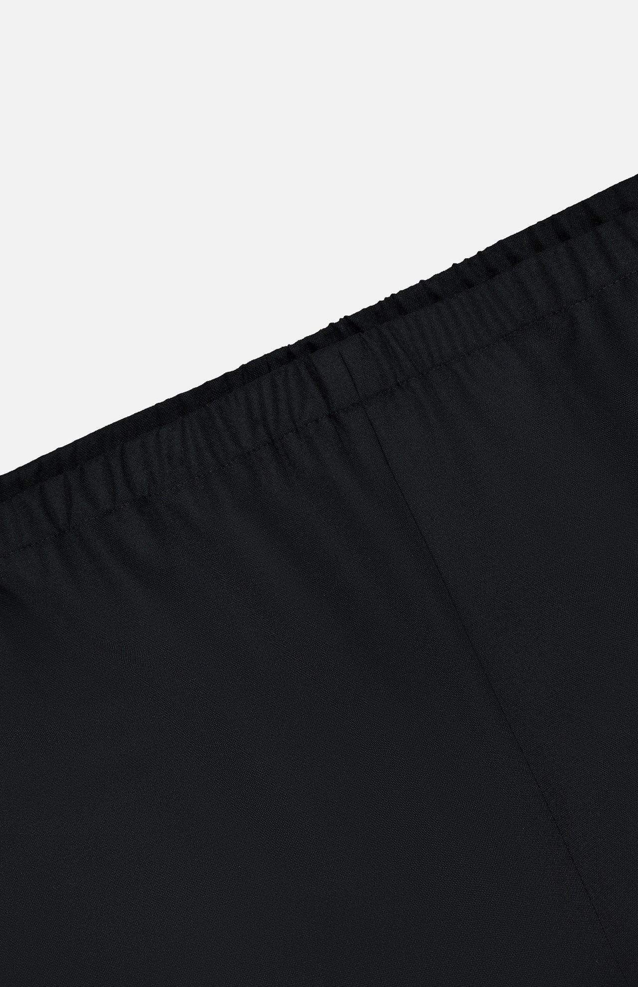 Close-up of the waistband on KHAITE's Roma Cropped Pull-on Pant in black, showing an elastic band and seam details. Made from lightweight wool suiting with a smooth, slightly shiny finish. Light gray background.